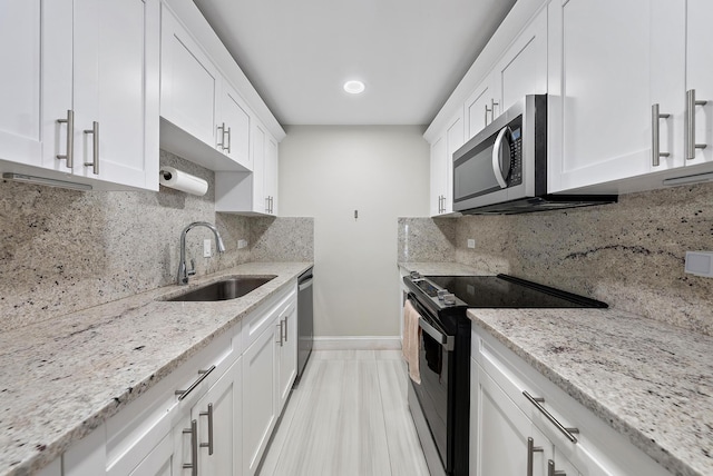 kitchen with light stone countertops, white cabinetry, stainless steel appliances, and a sink