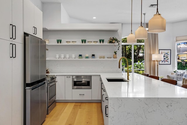 kitchen with light wood finished floors, a peninsula, a sink, stainless steel appliances, and white cabinets