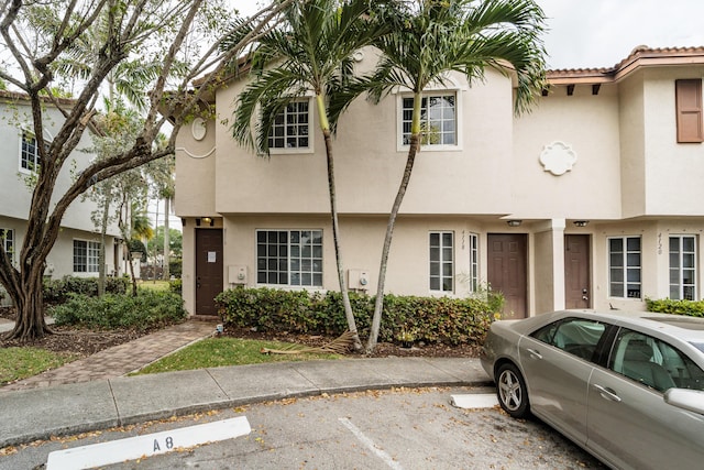 view of property with stucco siding, uncovered parking, and a tile roof