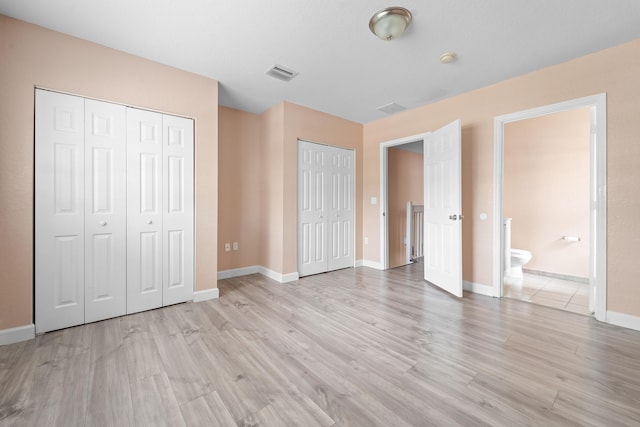 unfurnished bedroom with light wood-style flooring, baseboards, visible vents, and two closets