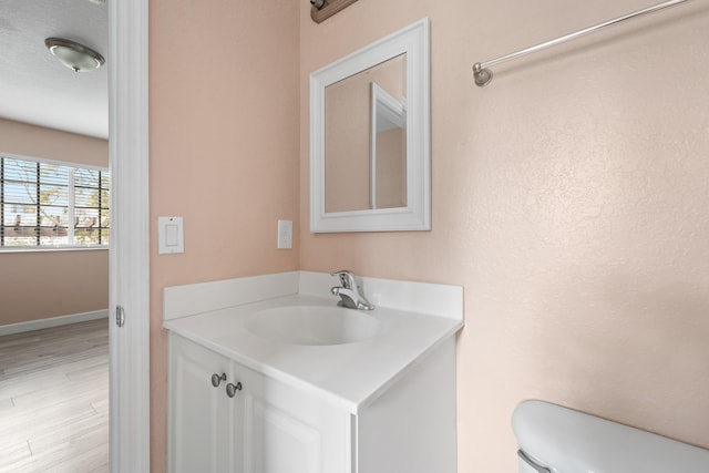 bathroom featuring baseboards, toilet, wood finished floors, and vanity