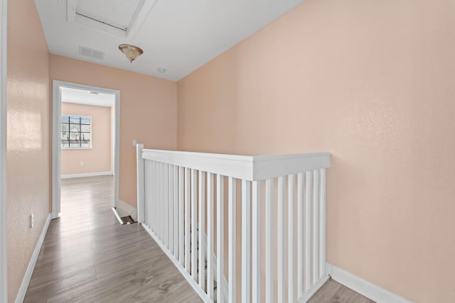 hall with wood finished floors, visible vents, and baseboards