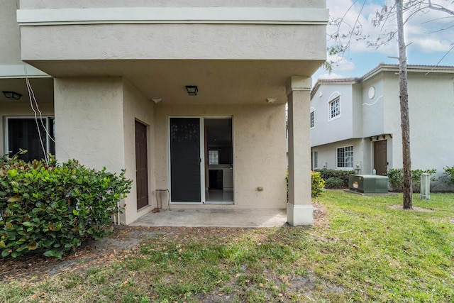 entrance to property featuring a patio area, stucco siding, central AC, and a yard