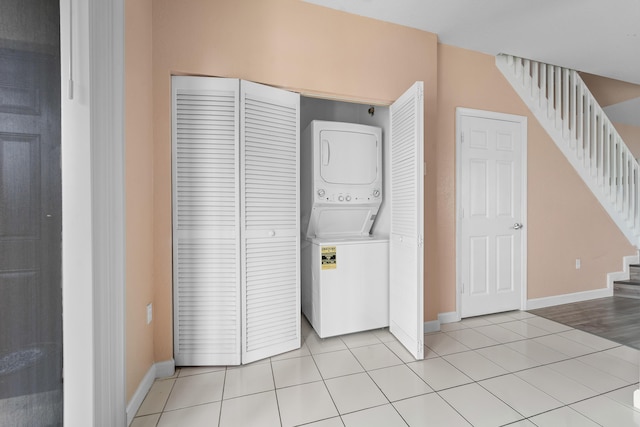 clothes washing area featuring laundry area, light tile patterned flooring, baseboards, and stacked washer and clothes dryer