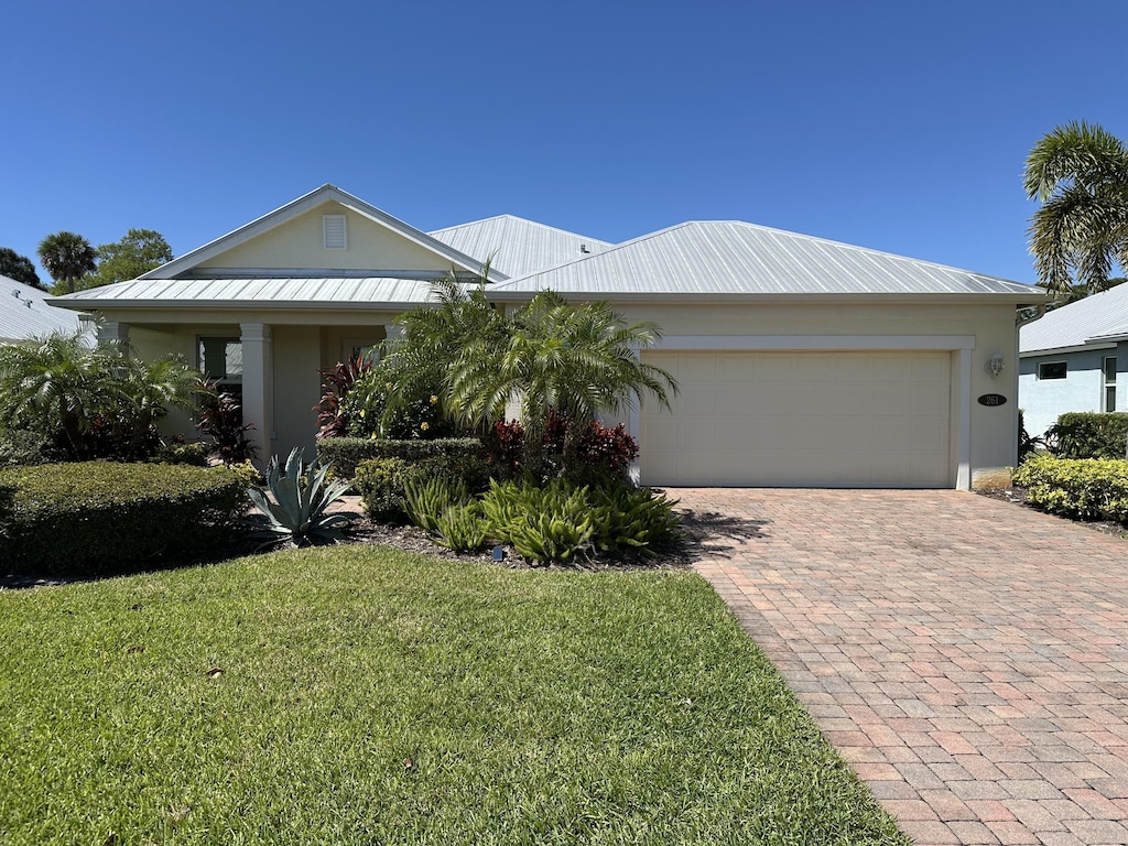 view of front of property featuring a standing seam roof, a front lawn, a garage, decorative driveway, and metal roof