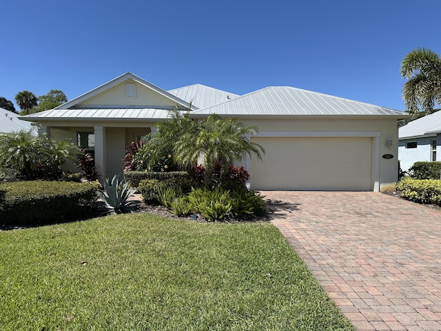 view of front of property featuring a standing seam roof, a front lawn, a garage, decorative driveway, and metal roof