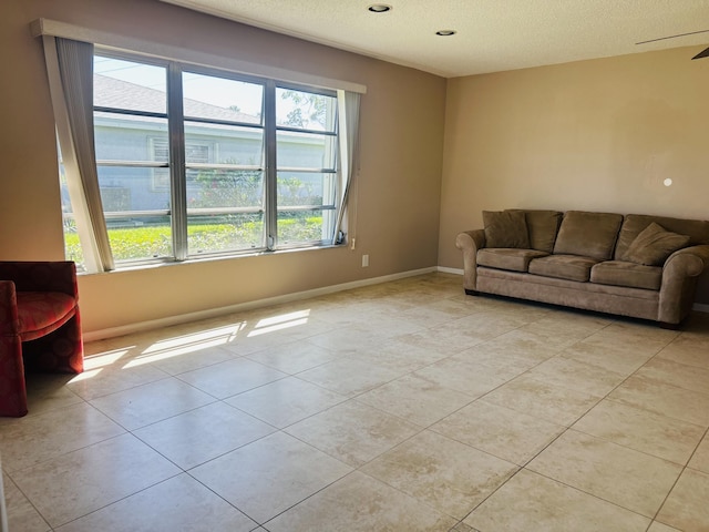 living room with ceiling fan, light tile patterned flooring, baseboards, and a textured ceiling