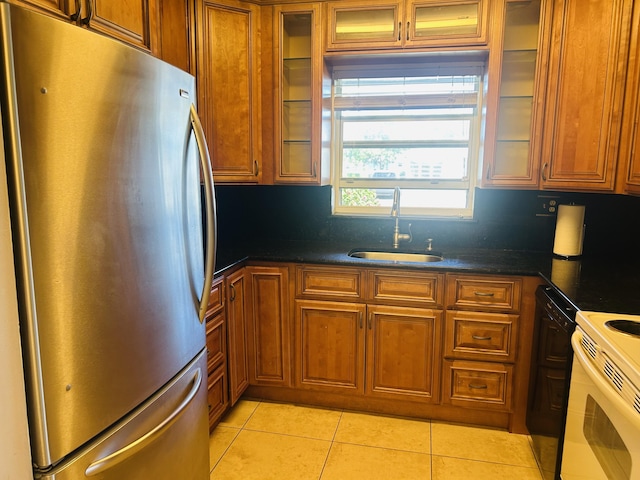 kitchen with white electric range oven, light tile patterned floors, brown cabinetry, freestanding refrigerator, and a sink