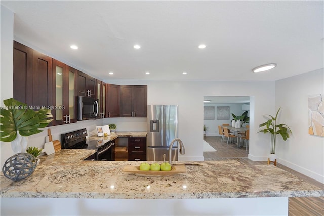 kitchen with electric range, stainless steel refrigerator with ice dispenser, dark brown cabinetry, glass insert cabinets, and light stone countertops