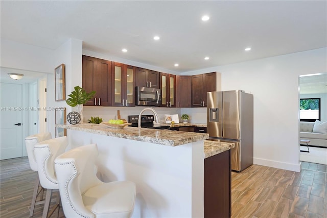 kitchen with stainless steel appliances, a kitchen breakfast bar, light wood-style floors, and a peninsula