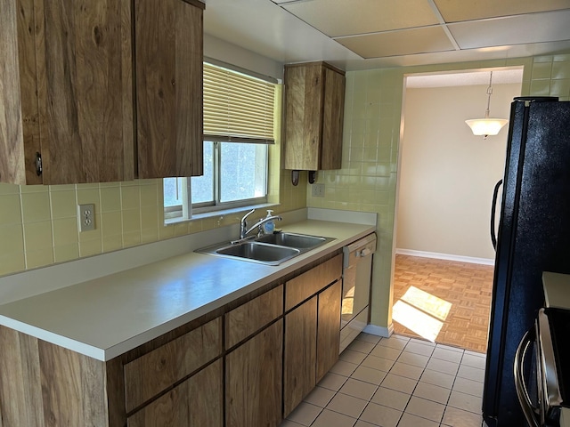 kitchen featuring a sink, backsplash, freestanding refrigerator, white dishwasher, and light countertops