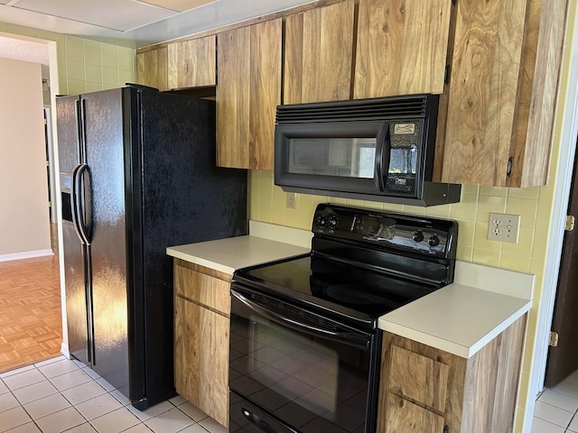 kitchen with light countertops, decorative backsplash, light tile patterned flooring, brown cabinetry, and black appliances