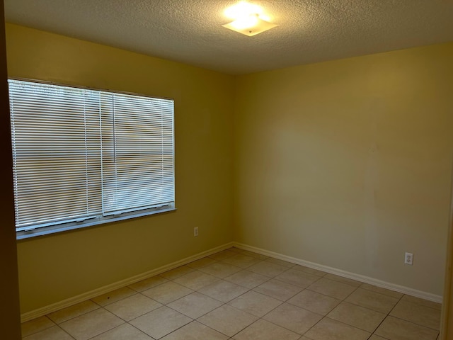 empty room with light tile patterned floors, baseboards, and a textured ceiling