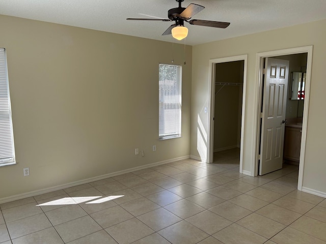 unfurnished bedroom with a walk in closet, a closet, light tile patterned floors, baseboards, and ceiling fan