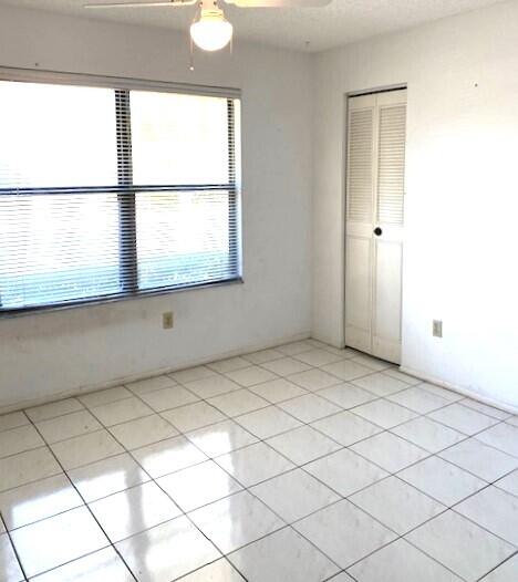 empty room with light tile patterned floors, plenty of natural light, and a ceiling fan