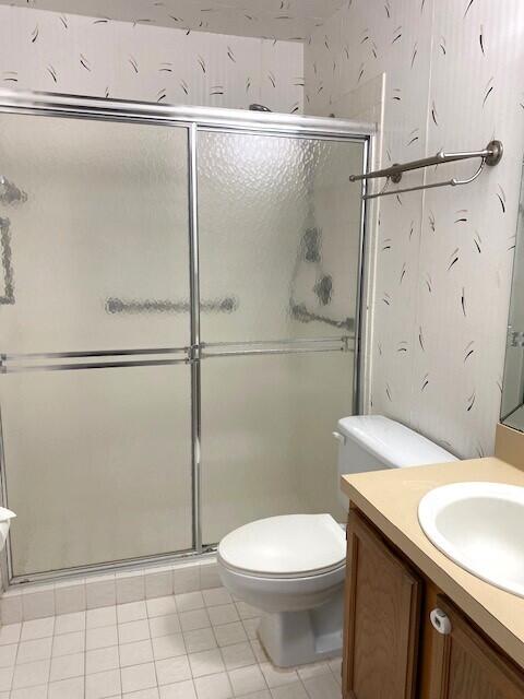 bathroom featuring toilet, a stall shower, vanity, and tile patterned flooring