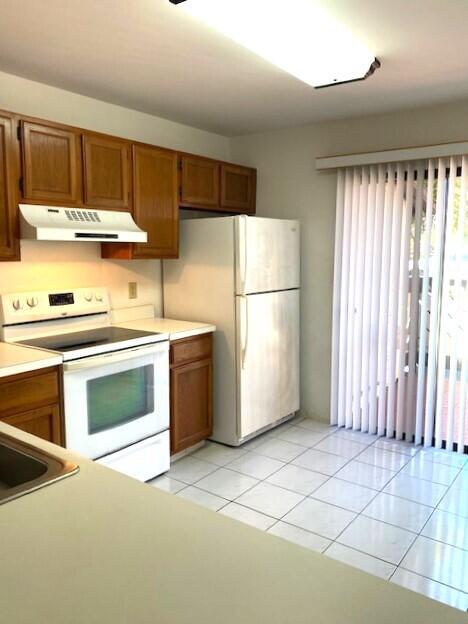 kitchen with under cabinet range hood, white appliances, brown cabinetry, and light countertops