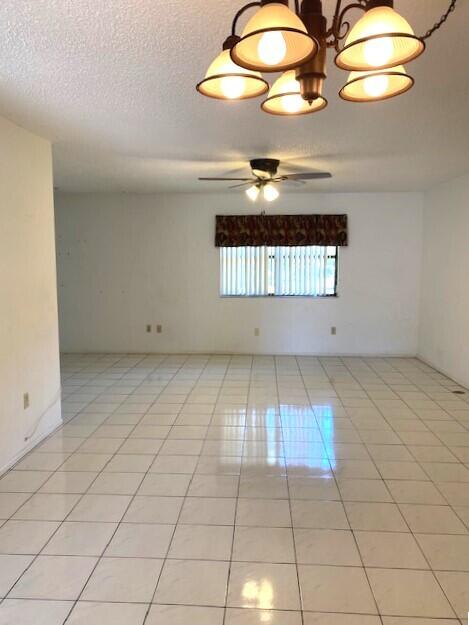 empty room featuring a textured ceiling, light tile patterned flooring, and ceiling fan