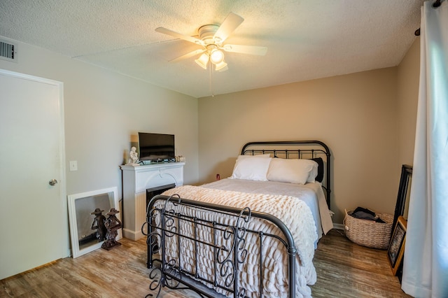 bedroom featuring ceiling fan, a textured ceiling, wood finished floors, and a fireplace