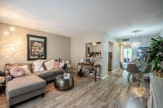 living area featuring a textured ceiling, baseboards, light wood-type flooring, and an inviting chandelier