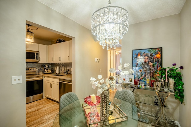 dining area with a notable chandelier, light wood finished floors, and a textured ceiling