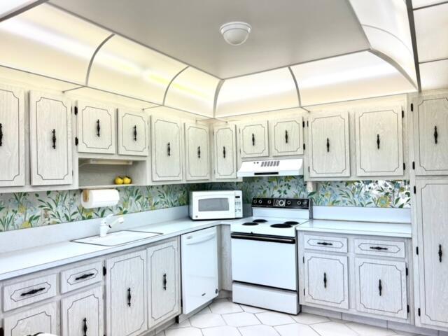 kitchen with white appliances, wallpapered walls, a sink, light countertops, and under cabinet range hood