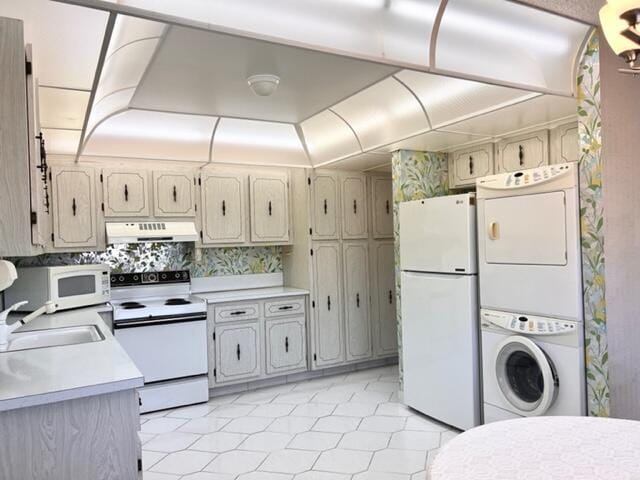 kitchen featuring white appliances, a sink, light countertops, stacked washer and clothes dryer, and under cabinet range hood