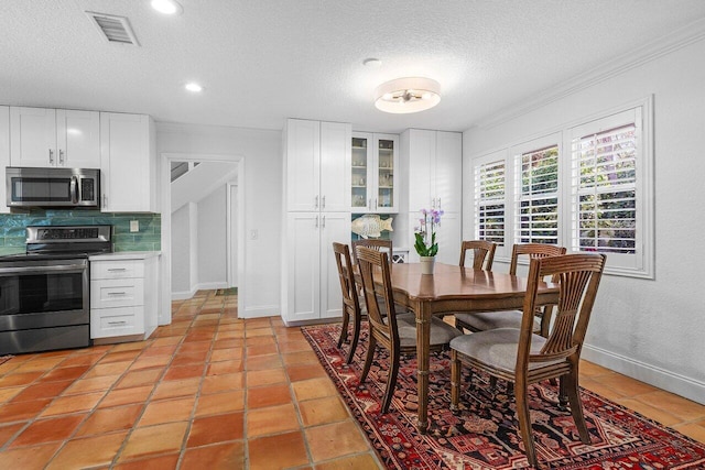 dining room featuring visible vents, a textured ceiling, light tile patterned flooring, crown molding, and baseboards