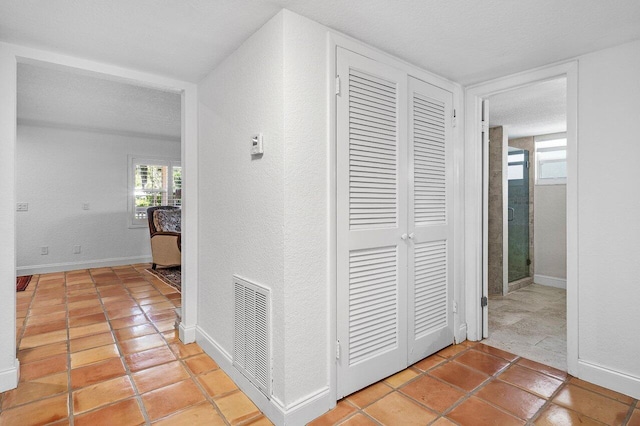 corridor with baseboards, visible vents, a textured wall, and a textured ceiling