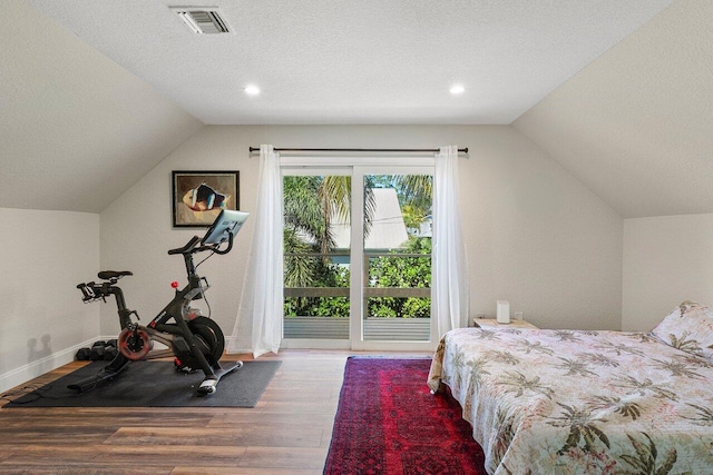 bedroom featuring wood finished floors, visible vents, vaulted ceiling, a textured ceiling, and access to outside