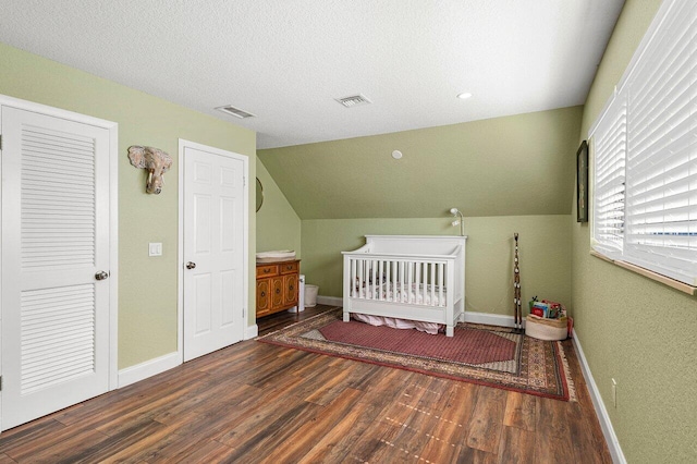 bedroom with visible vents, baseboards, vaulted ceiling, wood finished floors, and a textured ceiling