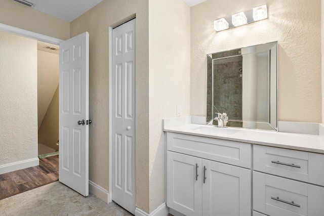 bathroom featuring baseboards, a textured wall, a tile shower, wood finished floors, and vanity