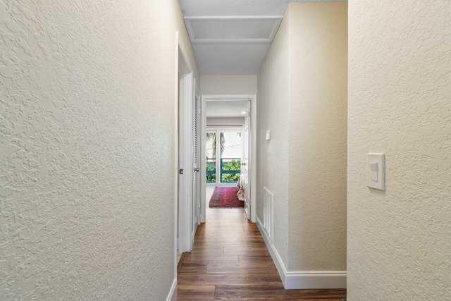 hall with wood finished floors, baseboards, and a textured wall