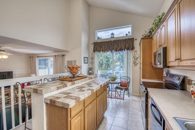 kitchen featuring light tile patterned floors, high vaulted ceiling, ceiling fan, a sink, and stainless steel appliances