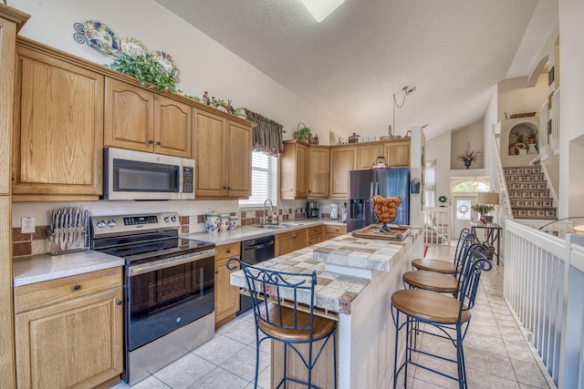 kitchen with a kitchen breakfast bar, a center island, appliances with stainless steel finishes, light tile patterned flooring, and vaulted ceiling