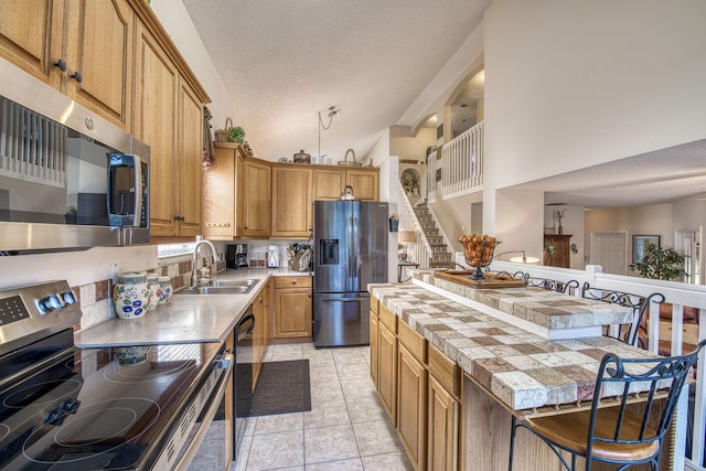 kitchen with a sink, a textured ceiling, appliances with stainless steel finishes, light tile patterned flooring, and vaulted ceiling