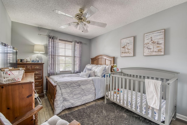 bedroom with ceiling fan, wood finished floors, baseboards, and a textured ceiling