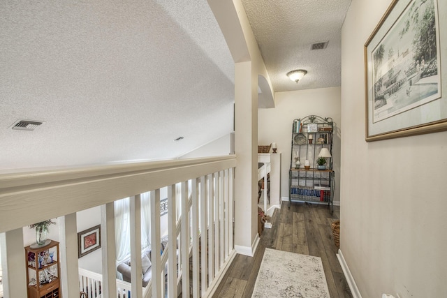 hallway with a textured ceiling, dark wood-style floors, visible vents, and baseboards