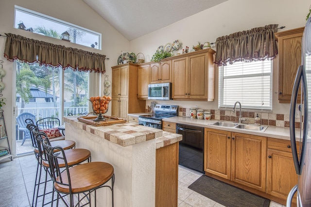 kitchen with a sink, stainless steel appliances, light countertops, vaulted ceiling, and a center island