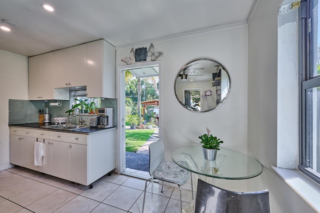 kitchen with tasteful backsplash, white cabinets, light tile patterned flooring, and a sink