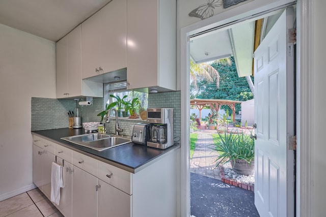 kitchen with dark countertops, decorative backsplash, white cabinets, and a sink