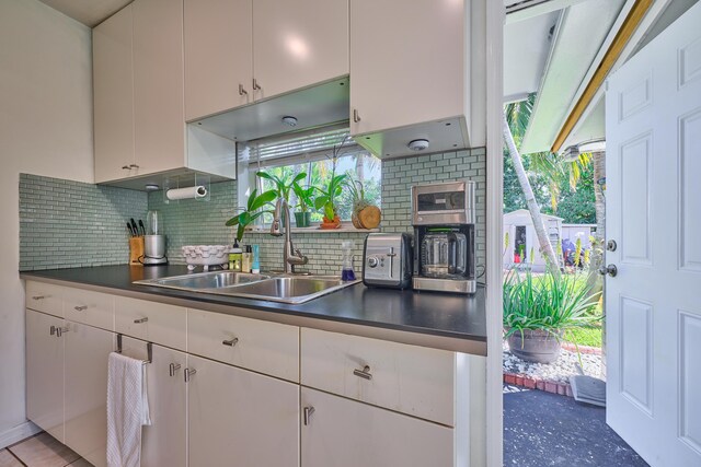 kitchen featuring tasteful backsplash, white cabinets, dark countertops, and a sink