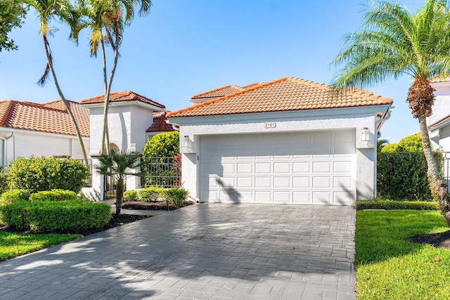 mediterranean / spanish house with a tiled roof, decorative driveway, an attached garage, and stucco siding