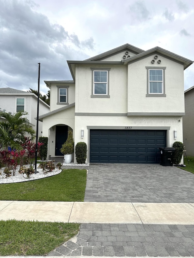 traditional home with stucco siding, decorative driveway, a front yard, and an attached garage