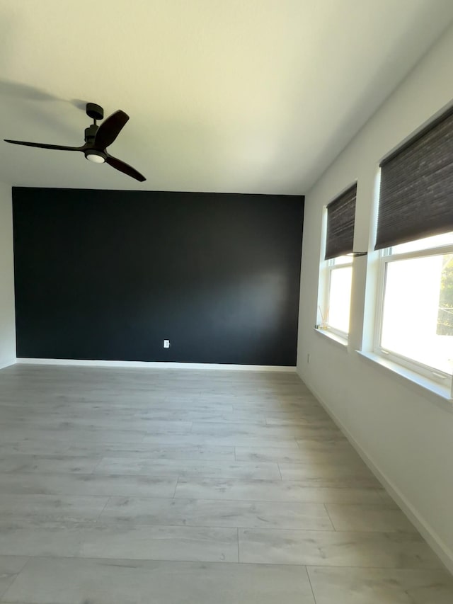 empty room with baseboards, ceiling fan, and light wood finished floors