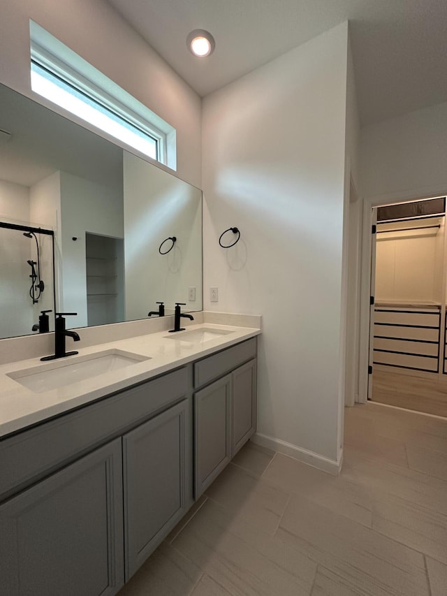 full bathroom featuring double vanity, baseboards, a shower stall, and a sink