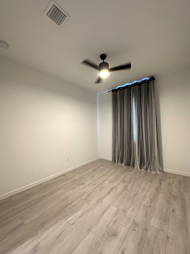 spare room with light wood-style flooring, a ceiling fan, visible vents, and baseboards