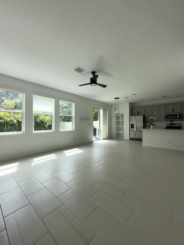 unfurnished living room with visible vents, a textured ceiling, and ceiling fan