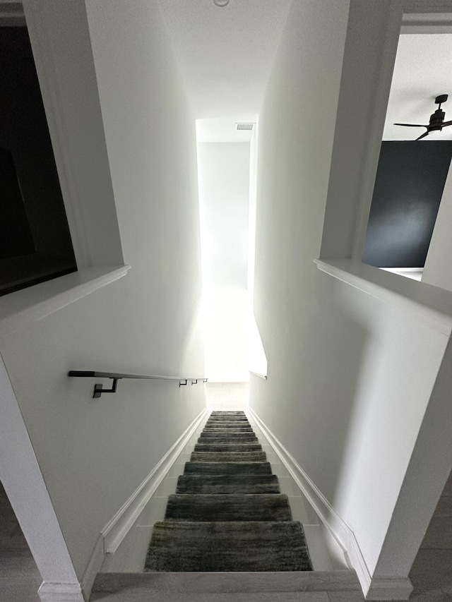 staircase featuring a ceiling fan and baseboards