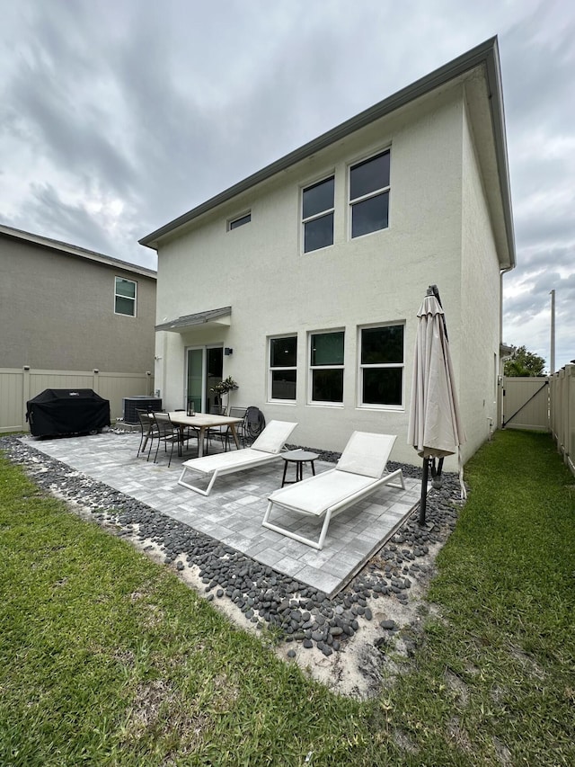 rear view of house with stucco siding, a fenced backyard, a yard, a patio area, and a gate